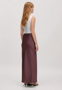 Lange, gladde, bordeaux satijnen rok gecombineerd met een witte tanktop. Heeft een aansluitende taille en loopt zachtjes uit naar de zoom.