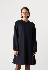 Donkerblauwe jurk met lange mouwen, ronde hals, een losse pasvorm en gathered cuffs. Heeft een gladde textuur en een minimalistisch ontwerp.