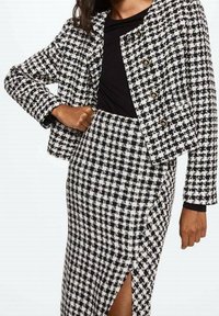 Blazer e gonna coordinati con motivo catenella in bianco e nero, caratterizzati da bottoni dorati, design corto e uno spacco alto fino al ginocchio nella gonna.