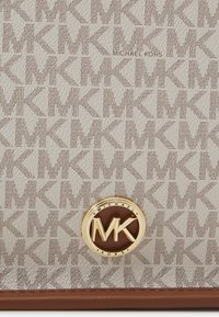 Michael Kors håndtaske med en tekstureret beige baggrund, der har et gentaget MK-logo mønster, samt et guld cirkulært emblem med brune accenter.