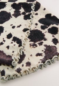 Black and beige ribbed fabric with a cow print pattern, featuring ruffled edges in a contrasting light color.