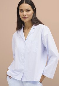 Camicia da pigiama a righe blu chiaro e bianche, con bottoni sul davanti, maniche lunghe e una singola tasca sul petto. Tessuto morbido con una sottile texture.