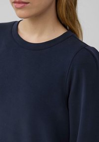 Marineblauer Pullover mit Rundhalsausschnitt, glatter Textur und gerafftem Schulterdetail, das ein einfaches, minimalistisches Design zeigt.