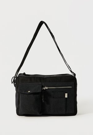 Sort rektangulær skuldertaske med lang rem, frontlomme med klap og knap, lynlåslomme og syede rektangulære rum.