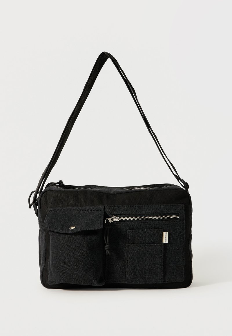 Μαύρη ορθογώνια τσάντα ώμου με μακριά λουράκι, μπροστινή τσέπη με καπάκι και κουμπί, τσέπη με φερμουάρ και ραμμένες ορθογώνιες θήκες.