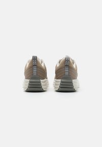 Un paio di scarpe sportive beige e grigie con suole bianche rigate, tasselli sul tallone grigi con punti riflettenti, viste da dietro su sfondo bianco.