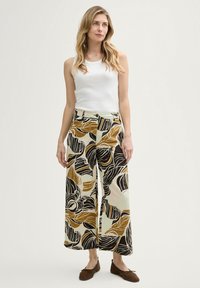 Pantalons à jambes larges en tissu léger avec un motif floral noir, doré et crème, associés à un débardeur blanc ajusté.