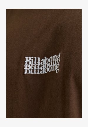Bézs színű, pamut póló, amelynek bal oldalán fehér hímzett szöveg olvasható "Billabong" felirattal, tükrözött, ismétlődő mintázatban.
