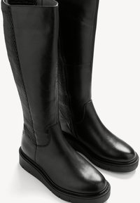 Fekete, térdig érő csizmák sima bőrből és texturált hálós panelekből, kerek orral és lapos gumitalppal.