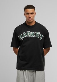 Svart bomulls t-skjorte med fet hvit og grønn "MARKET" tekst. Klassisk design med korte ermer og rund hals.