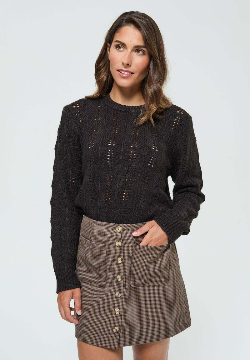 Pull noir en tricot avec un motif texturé et manches longues, associé à une jupe écossaise marron dotée de poches avant et d'une fermeture à boutons.