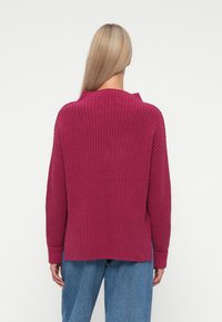 Sweater malva tricotado com um corte descontraído, apresentando textura canelada, mangas longas e uma bainha ligeiramente curva. Usado com jeans azul claro.