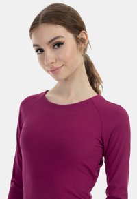Ljus magenta långärmad topp med ribbad textur. Har en rund halsringning och raglansärmar, figurnära silhuett.