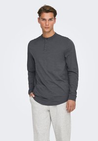 Donkergrijs henley shirt met lange mouwen, een ronde hals, een drieknopenbies en geribbelde manchetten, gecombineerd met lichtgrijze joggingbroek.