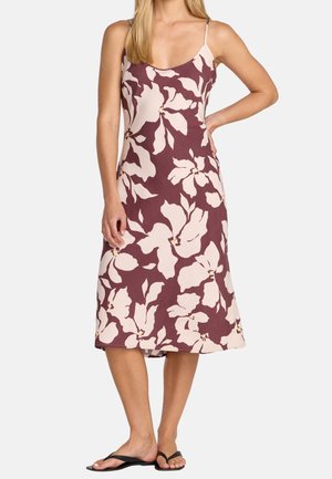 Kvinde iført en ærmeløs, burgunderfarvet midi-kjole med store lyserøde blomsterprint og sorte flip flop-sandaler.
