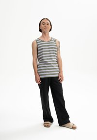 Grau-weiß gestreifes Tanktop mit abgerundetem Saum, kombiniert mit schwarzen weiten Hosen und beigen Schippersandalen. Einfaches Design, lässiger Look.