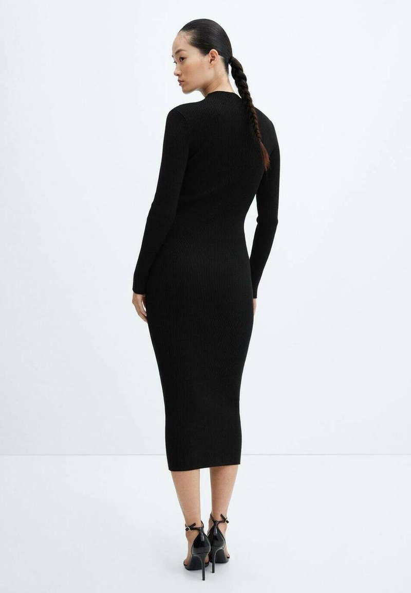 Abito midi nero a costine con maniche lunghe e una silhouette attillata, caratterizzato da un collo alto e una texture liscia. Abbinato a tacchi neri.