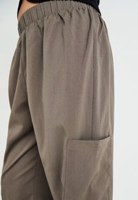 Lagane, hlače boje khaki s elastičnom trakicom u struku i jednim bočnim džepom. Glatka tekstura i opušteni kroj.