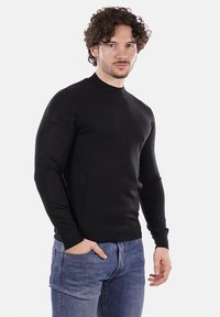 Maglione nero lavorato a maglia con maniche lunghe e collo alto. Design aderente con polsini e orlo a costine, abbinato a jeans in denim blu.
