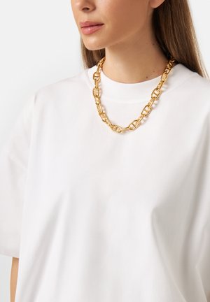 T-shirt blanc à manches courtes avec un col rond, associé à un collier en chaîne dorée épaisse avec de grands segments liés.
