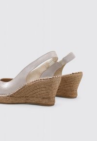 Sandalias de cuña con un acabado plateado brillante, tira de textil en el talón y tacón de yute trenzado en color beige. Presentan una punta redondeada y una textura sutil.
