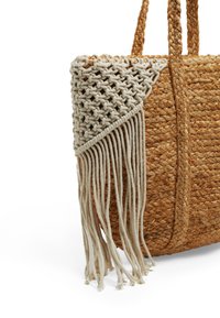 Borsa a spalla intrecciata in paglia con un design in macramè creme e frange su un lato; presenta manici intrecciati e un corpo spazioso e textured.