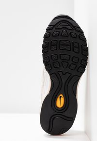 Semelle d’une chaussure de sport noire et blanche avec une bande de roulement texturée et un ovale jaune comportant un logo swoosh noir au centre.
