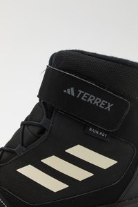 Czarne buty trekkingowe z wytrzymałym materiałem wierzchnim, regulowanym paskiem na rzep oraz trzema białymi skośnymi paskami po boku.