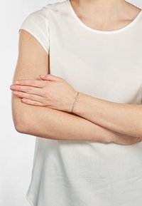 Silbernes Armband mit blattartigen Gliedern und gleitender Oberfläche, getragen an einem Handgelenk mit heller Hautfarbe, vor einem schlichten weißen Hintergrund.