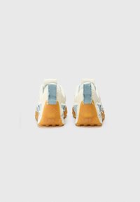 Des baskets blanches et bleues avec un design texturé, dotées d'une semelle en caoutchouc, d'une languette à l'arrière et de détails de couture visibles.