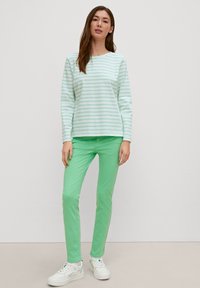 Zielona koszula w paski z długim rękawem, w białe linie, w zestawie z jednolitymi, zielonymi spodniami typu slim fit oraz białymi sneakersami. Prosty, codzienny strój.