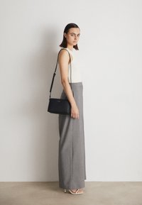 Černá crossbody taška se hladkým povrchem, s dlouhým popruhem. Nositá s ribovaným bílým topem a šedými kalhotami s vysokým pasem.