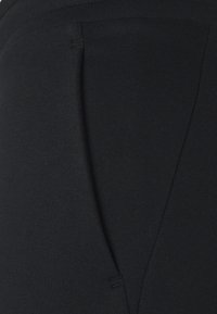 Černé tepláky z měkké bavlněné směsi, s přehlou siluetou nohavic a jemnými švy. Bez viditelných kapes.