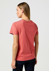 Kurze Ärmel, korallenfarbenes T-Shirt aus weichem Stoff. Verfügt über einen Rundhalsausschnitt mit normaler Passform und glatter Textur.