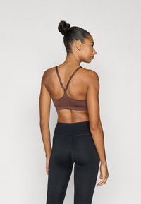 Καφέ αθλητικό σουτιέν με ρυθμιζόμενους ιμάντες, με σχεδιασμό πίσω με στρογγυλεμένο κόψιμο. Συνδυάζεται με μαύρο ψηλόμεσο κολάν. Ομαλή υφή υφάσματος.