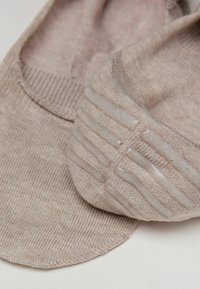 Béžové bavlněné ponožky s texturovaným protiskluzovým vzorem na patě a žebrovanými lemy. Hladký povrch, bez viditelných švů.