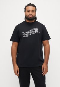 Sort bomulds-T-shirt med hvidt grafisk tryk, rund hals og korte ærmer, båret af en mand, der står oprejst.