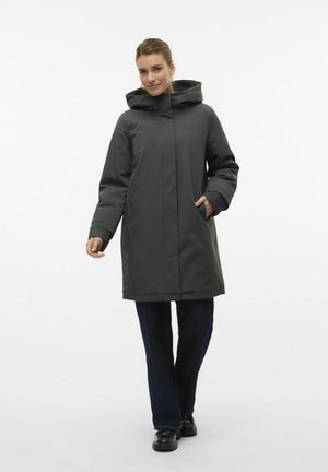 Donkergrijze weersbestendige jas met een capuchon, voorvakken en een rechte snit, gecombineerd met donkerblauwe jeans en zwarte schoenen.