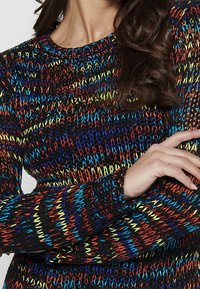 Meer kleurige gebreide trui met een zwarte basis en levendige blauwe, gele en rode strepen. Getextureerde, lange mouwen met een ronde halslijn.