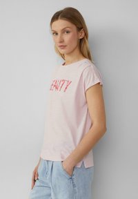 Lichtroze T-shirt met korte, opgerolde mouwen en "BEAUTY" in rode letters. Zachte, lichte stof met zijsplitten voor een gemakkelijke beweging.