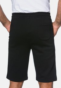 Pantalones cortos deportivos negros con cinturilla elástica, corte hasta la rodilla y un único bolsillo trasero. Textura suave sin patrones visibles.