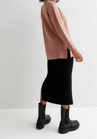 Maglione a maglia rosa chiaro con maniche lunghe, fessure laterali, abbinato a una gonna nera e stivali neri alla caviglia con suola spessa.