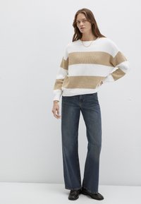 Gestreifter Pullover in Weiß und Beige, Oversize-Passform mit gerippter Struktur, kombiniert mit hoch taillierten Jeans und schwarzen Loafers.