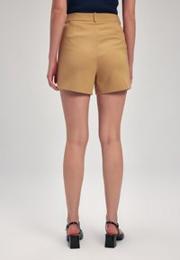 Kaki skræddersyede shorts med høj talje og flad front. Glat stof, skrå lommer og en baglomme detalje. Båret med sorte hæle sandaler.