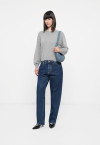 Suéter de punto gris de manga larga, jeans de cintura alta azules, bailarina negra de punta y un pequeño bolso de hombro azul. Fondo liso.