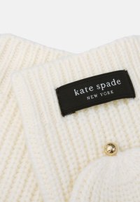 Hvid ribbet strikscarf med et sort mærke med "kate spade NEW YORK" i hvid tekst og en guldbutton detalje.