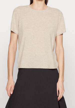 Donna indossa un top beige a maniche corte in maglia abbinato a una gonna nera a vita alta, vista dal collo ai fianchi su uno sfondo chiaro.