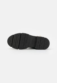 Suela de zapato de goma negra con un patrón de tracción texturizado, que presenta profundos surcos y un logotipo circular rebajado. Material liso y duradero.