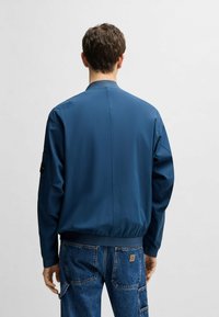 Blauer Bomberjacke aus leichtem Material, mit einem gerippten Kragen und Bündchen, glatter Oberfläche und ohne sichtbare Muster.