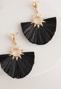 Black fan-shaped earrings made of textured material, featuring gold-toned sunburst accents and a central cutout.